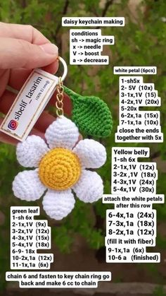 a crocheted keychain with a white flower and green leaves on it