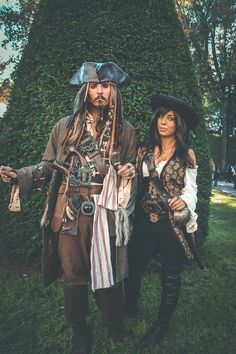 two people dressed up as pirates standing next to each other in front of a hedge