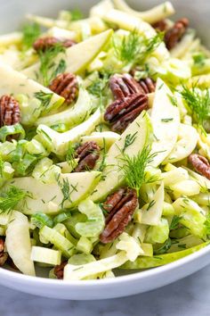 a white bowl filled with apple and fennel salad on top of a marble counter