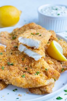 fried fish with lemon and parsley on a white plate next to two small cups