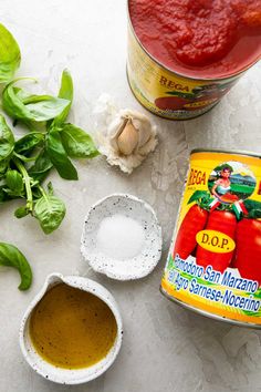 ingredients to make homemade marinara sauce laid out on a white surface with basil and garlic