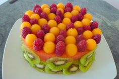 a fruit cake with kiwis, oranges and raspberries on top