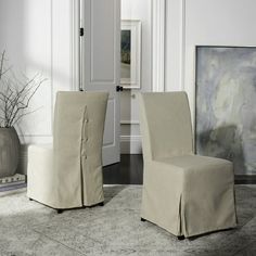 two beige chairs sitting next to each other in front of a painting on the wall