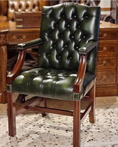 a green leather chair sitting on top of a tile floor next to a wooden desk