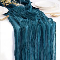 the table is set with plates, silverware and a teal colored cloth draped over it