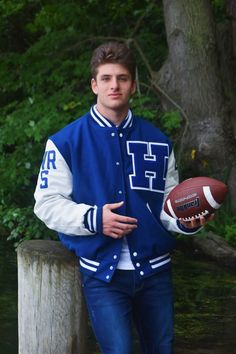 a young man is holding a football and posing for a photo in front of some trees