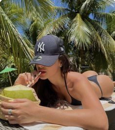 a woman laying on top of a hammock next to palm trees drinking a drink