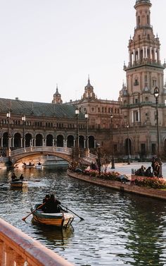 people are riding in small boats on the water next to a bridge and large buildings