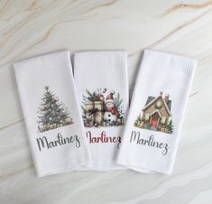 three white kitchen towels with houses and christmas trees on them