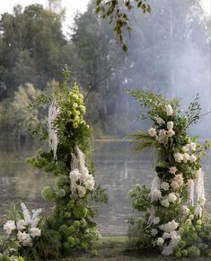 an outdoor ceremony setup with flowers and greenery on the side of a body of water