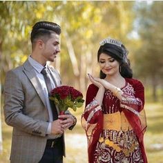 a man standing next to a woman in a red and yellow dress holding flowers on her hand