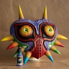 a colorful mask with spikes on it next to a bottle of glue and a brown background