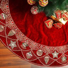 a christmas tree skirt with ornaments on it and a red velvet table cloth around it