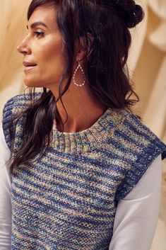 a woman wearing a sweater and earrings looking off to the side with her hand on her hip