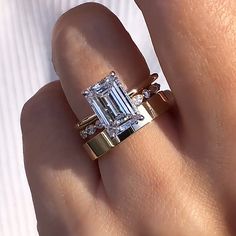 a woman's hand with a diamond ring on top of her finger and an emerald stone in the middle