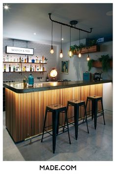 a bar with three stools in front of it and lights hanging from the ceiling