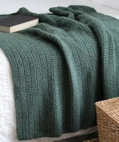 a green blanket sitting on top of a bed next to a wicker basket filled with books