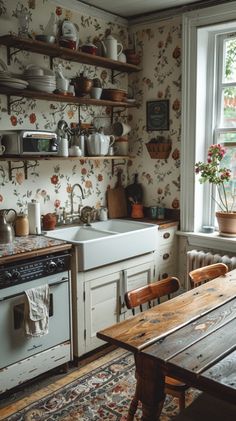 an old fashioned kitchen with floral wallpaper and wooden table in the foreground, open shelving above