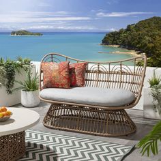 an outdoor seating area overlooking the ocean and tropical plants on a sunny day with blue water in the background