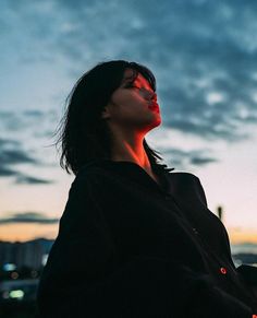 a woman with her eyes closed standing in front of the sky at sunset or dawn