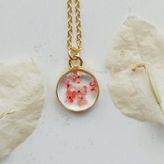 a necklace with flowers on it sitting next to a piece of paper and a plant