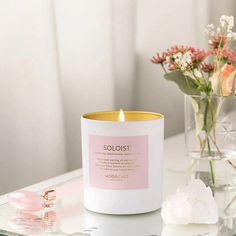 a white candle sitting on top of a table next to some pink flowers and glass vases