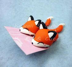 two small orange and white foxes sitting on top of a pink piece of paper