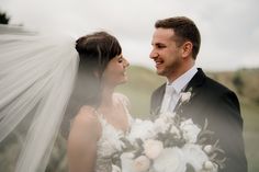 the bride and groom are looking at each other while posing for a wedding photo with their veil blowing in the wind