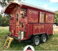 a red and gold painted horse trailer parked in the grass