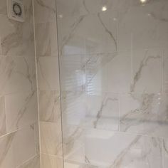 a bathroom with white marble tile walls and floor, along with a walk in shower