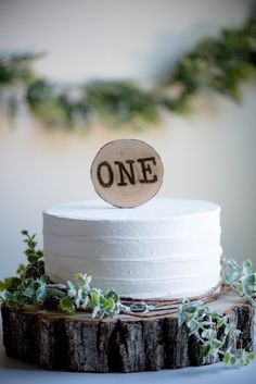 a white cake sitting on top of a wooden slice with the word one written on it