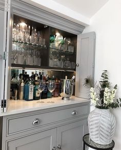 a bar with wine glasses and liquor bottles on the top shelf next to a vase filled with flowers