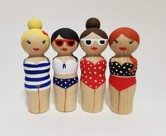 four wooden dolls are standing next to each other on a white surface, wearing swimsuits and sunglasses