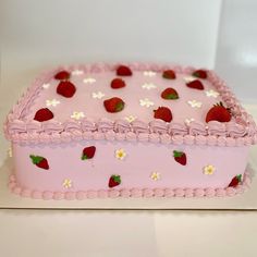 a pink cake decorated with strawberries and daisies on a white tableclothed surface