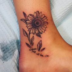 a sunflower tattoo on the foot with words written in cursive writing below it