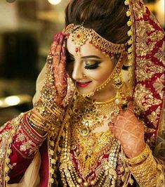 a woman in a red and gold bridal outfit holding her hands up to her face