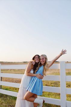 two women standing next to each other in front of a white fence