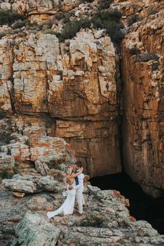 a bride and groom standing on the edge of a cliff