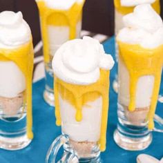 there are many desserts in glass cups on the blue tablecloth with white and yellow icing