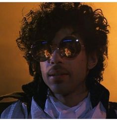 a young man with curly hair and sunglasses looking off to the side in front of an orange wall