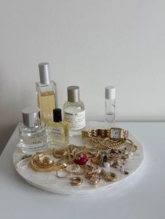 an assortment of perfumes and jewelry on a marble tray with white walls in the background