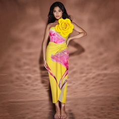 a woman in a yellow and pink dress with a flower on her head is posing for the camera