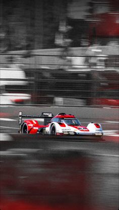 a red and white race car driving on a track with blurry buildings in the background