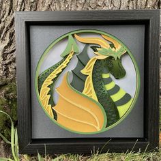 a green and yellow dragon cutout in a shadow box on the ground next to a tree