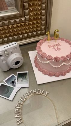 a pink birthday cake sitting on top of a table next to pictures and a camera