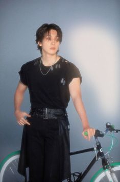 a man standing next to a bike with his hands on the handlebars and wearing a black shirt