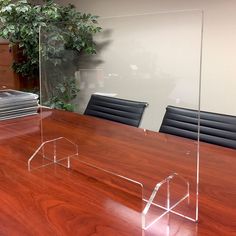 a clear acrylic desk with black chairs and a plant in the corner behind it