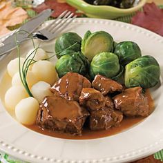 a white plate topped with meat and brussel sprouts next to potatoes