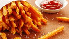 french fries with ketchup and salt on a wooden table next to dipping sauce