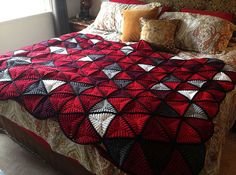 a bed with a red and black quilt on it's headboard next to a window